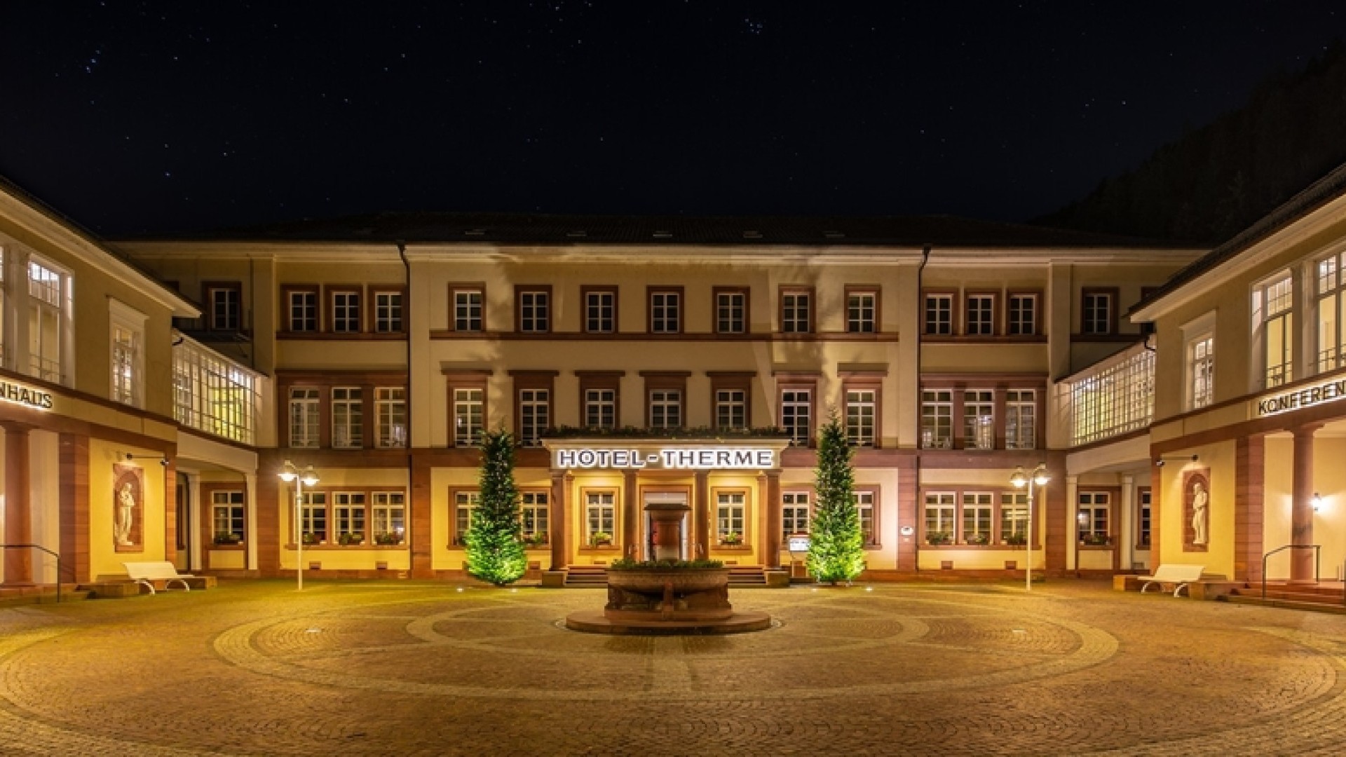 Beleuchteter Innenhof des Hotels Therme Bad Teinach bei Nacht mit Springbrunnen und Konferenzhaus