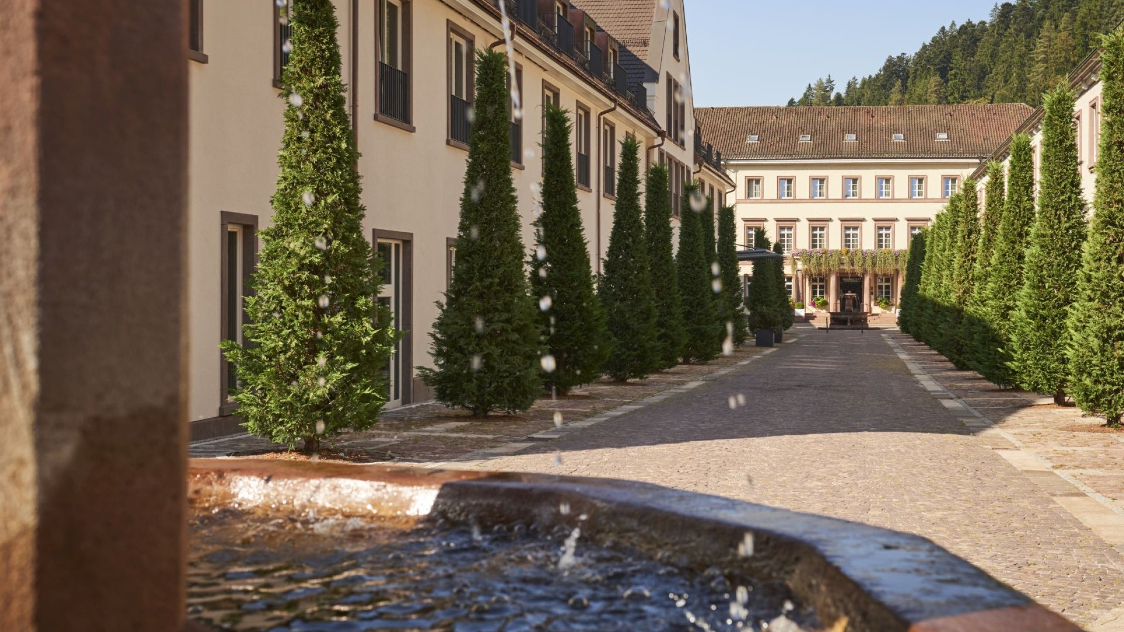Blick auf den Hotelinnenhof mit Wasserbrunnen und symmetrischer Baumallee