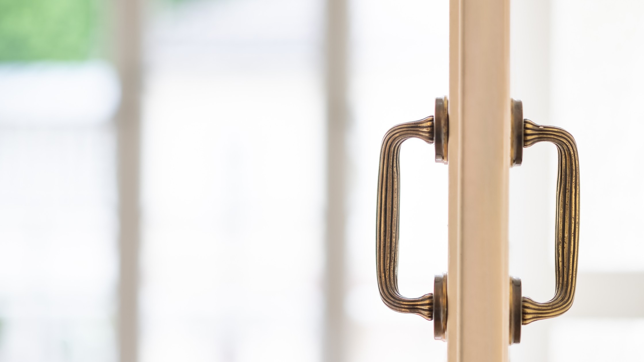 Detailaufnahme eines goldfarbenen Türgriffs vor heller Fensterfront