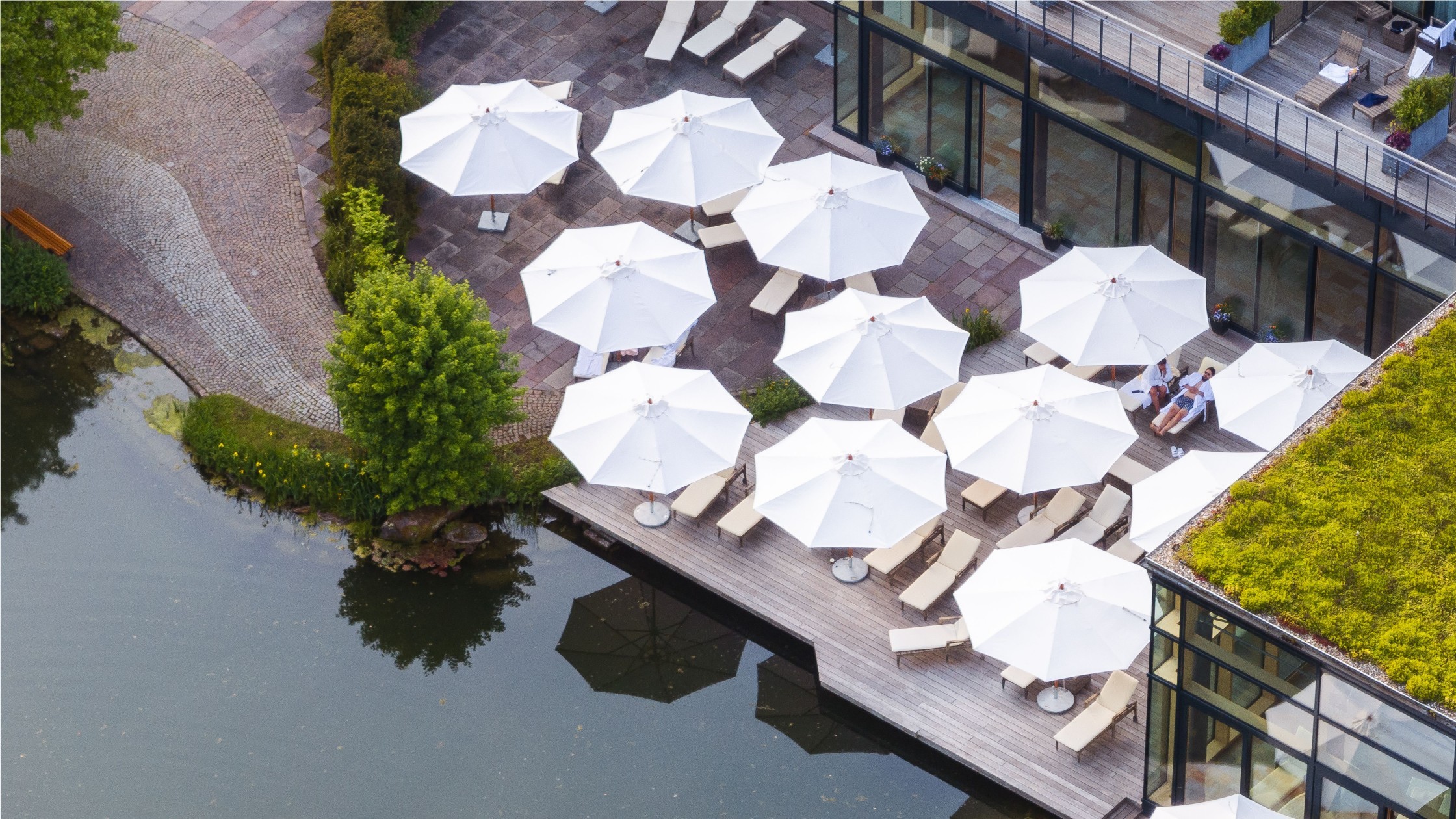 Sonnenterrasse am Wasser mit weißen Sonnenschirmen und Liegen am Hotelpool