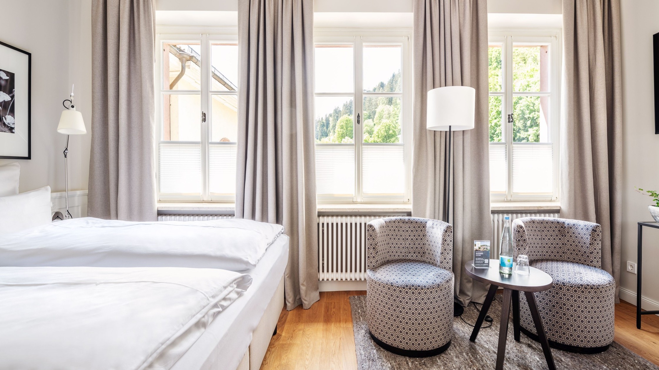 Freundliches Doppelzimmer mit großen Fenstern, gemütlichen Sesseln und hellem Interieur