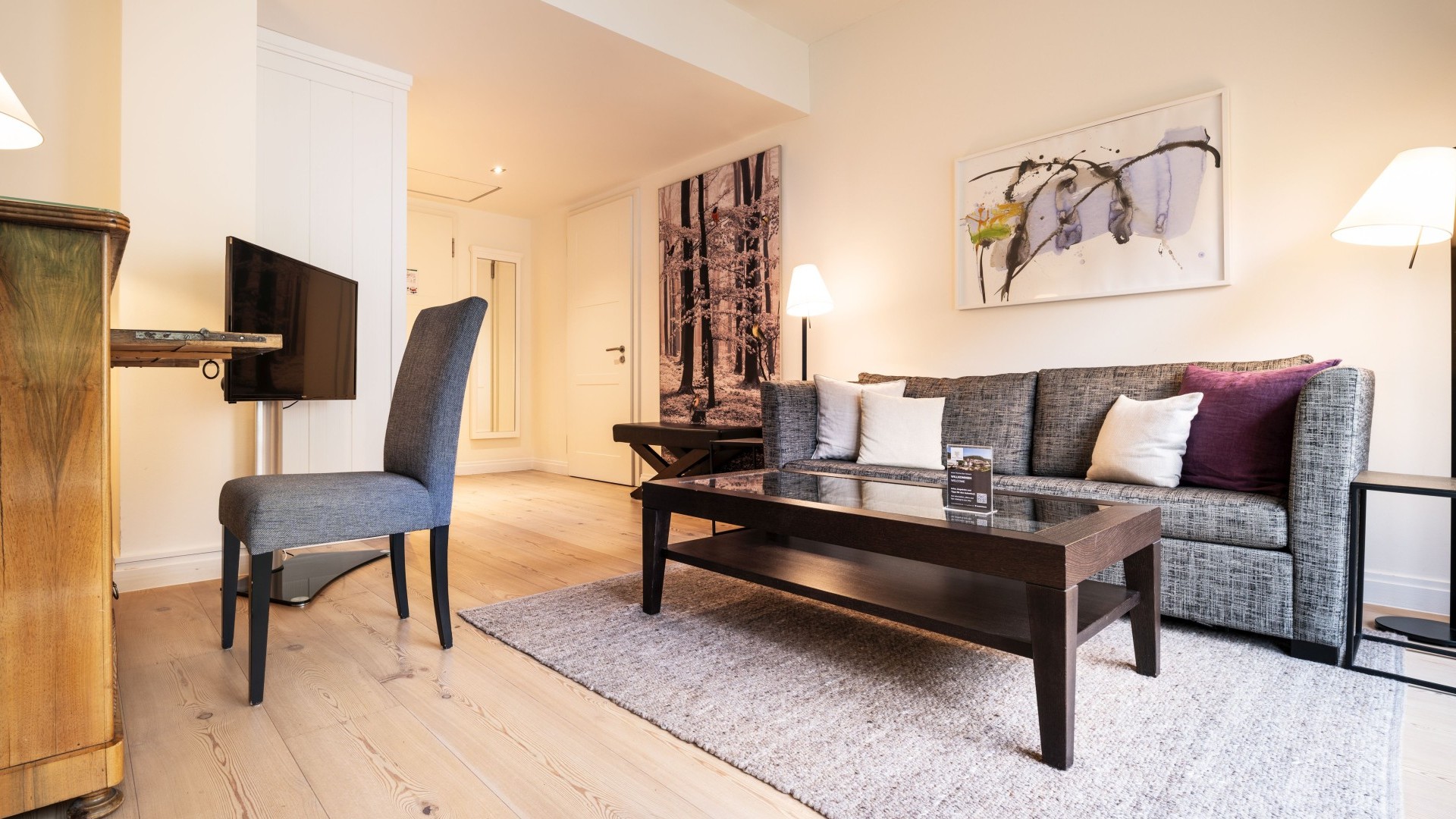 Helles Wohnzimmer mit grauem Sofa, Glastisch und stilvollen Wandbildern