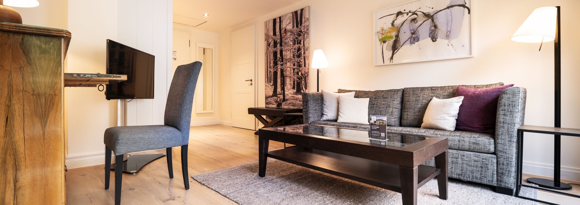 Helles Wohnzimmer mit grauem Sofa, Glastisch und stilvollen Wandbildern