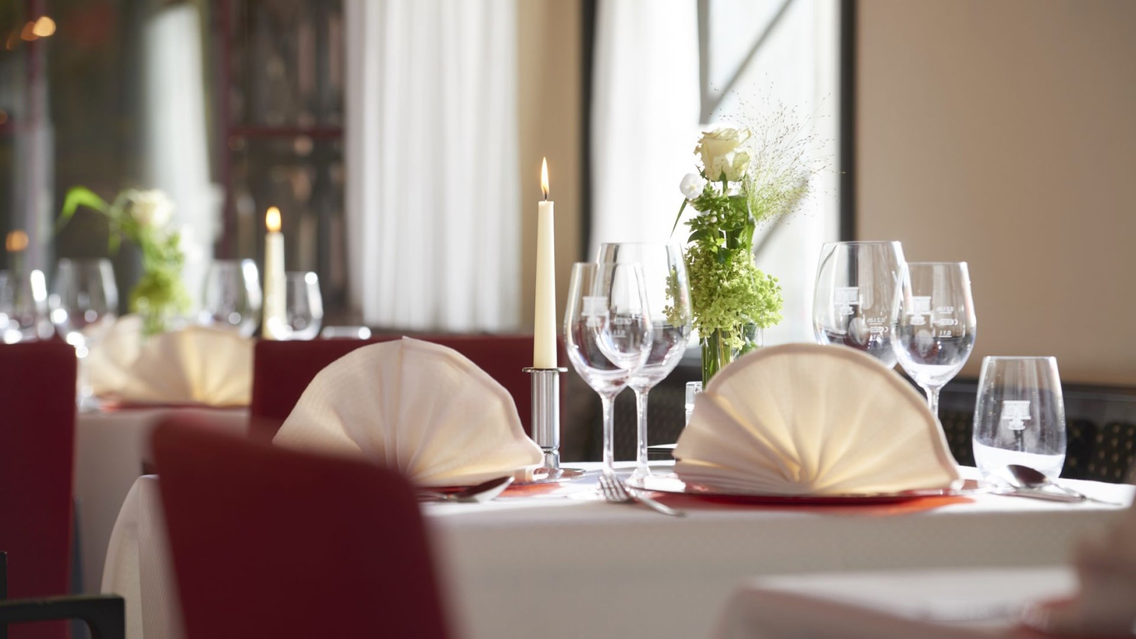 Elegant gedeckter Restauranttisch mit gefalteten Servietten, Kerze, Gläsern und Blumendeko