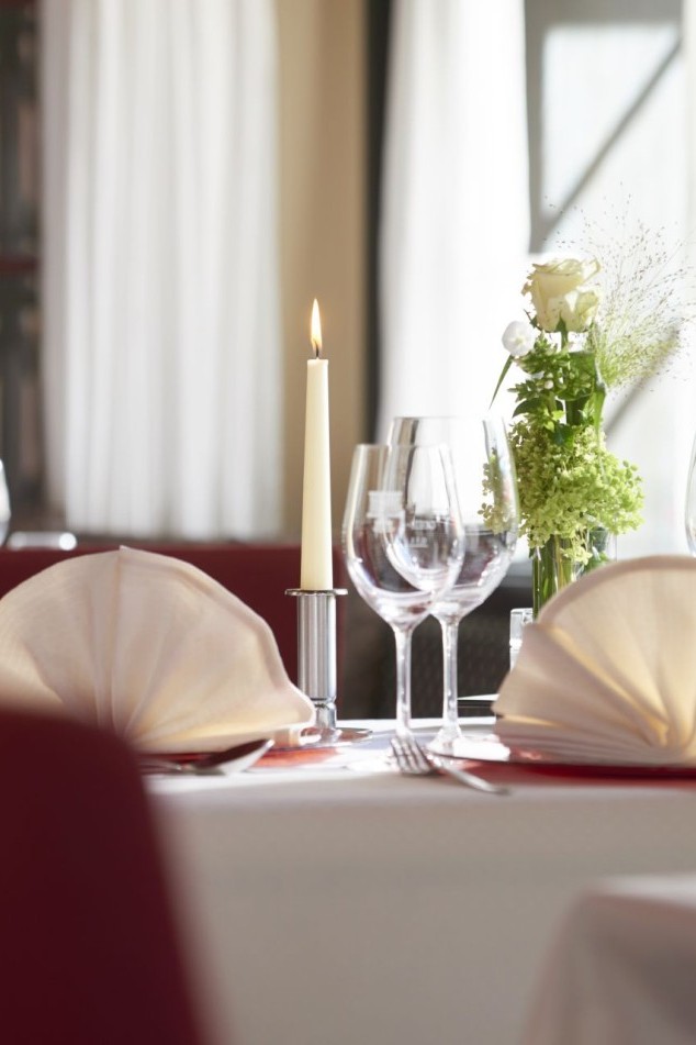 Elegant gedeckter Restauranttisch mit gefalteten Servietten, Kerze, Gläsern und Blumendeko