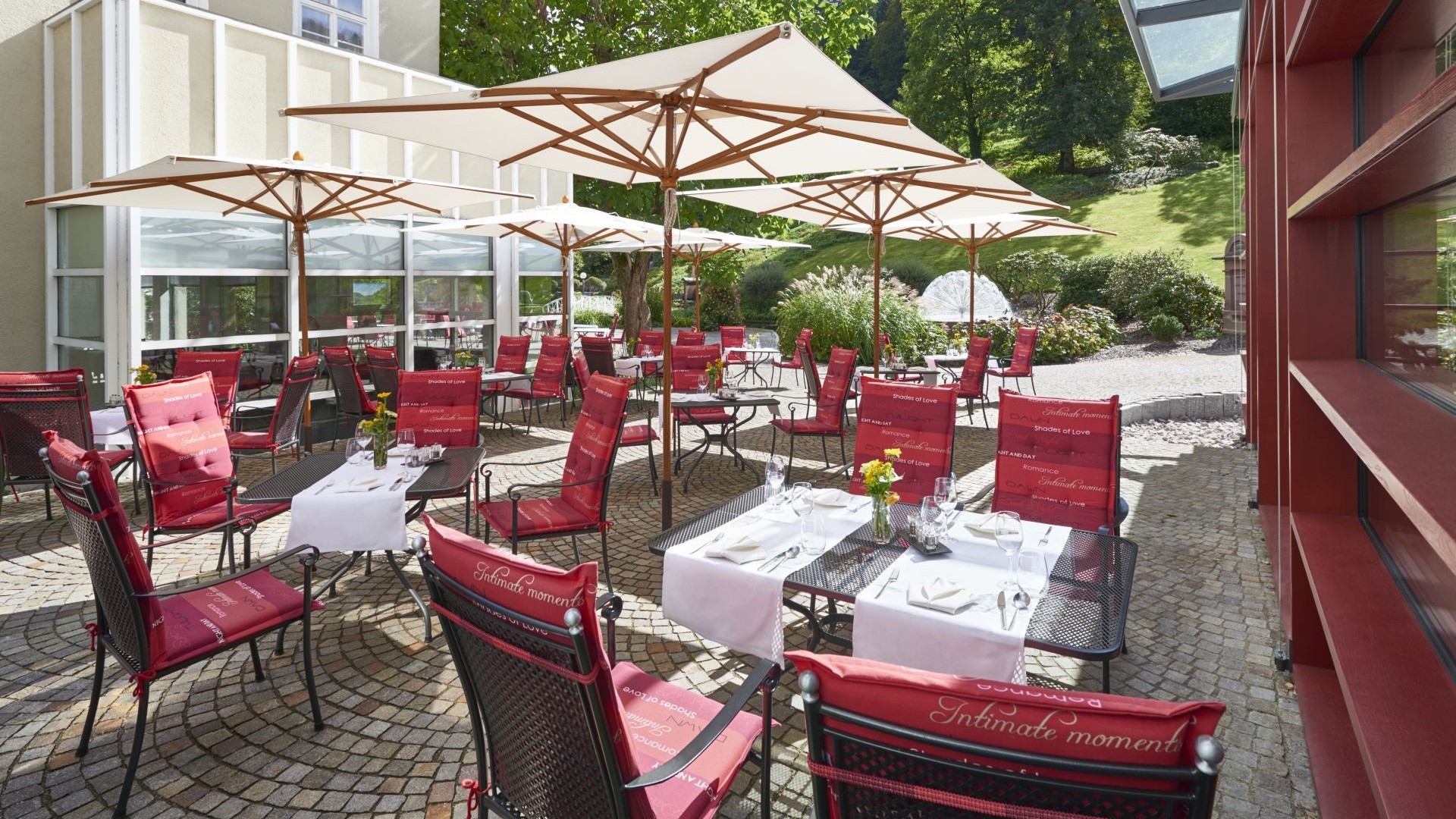 Sonnenterrasse mit gedeckten Tischen und roten Stuhlkissen