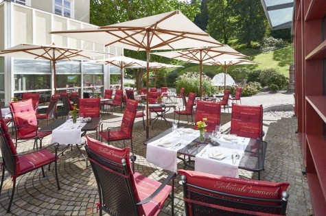 Sonnenterrasse mit gedeckten Tischen und roten Stuhlkissen