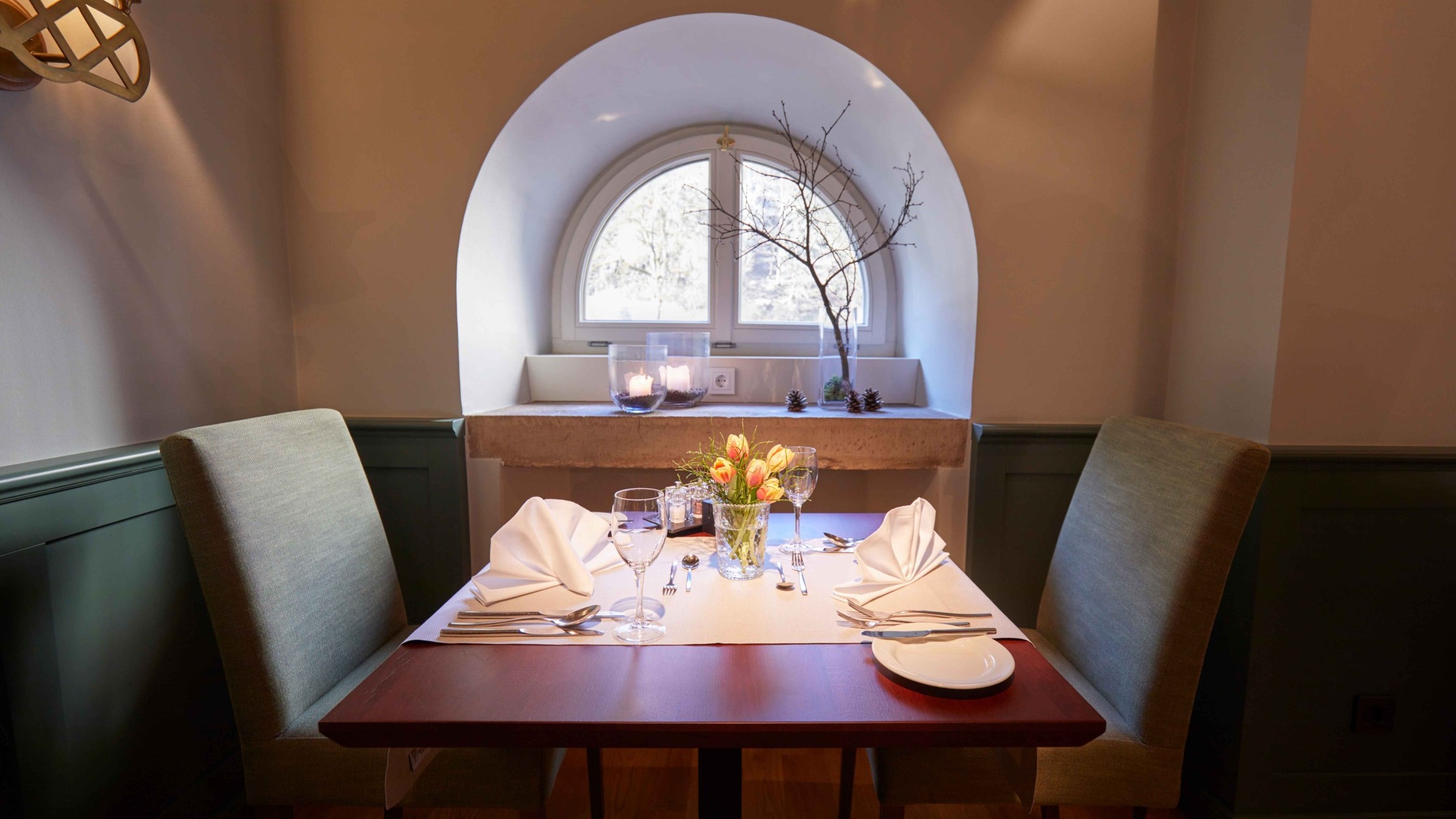 Liebevoll gedeckter Tisch für zwei Personen mit Blick auf ein rundes Fenster und Kerzen