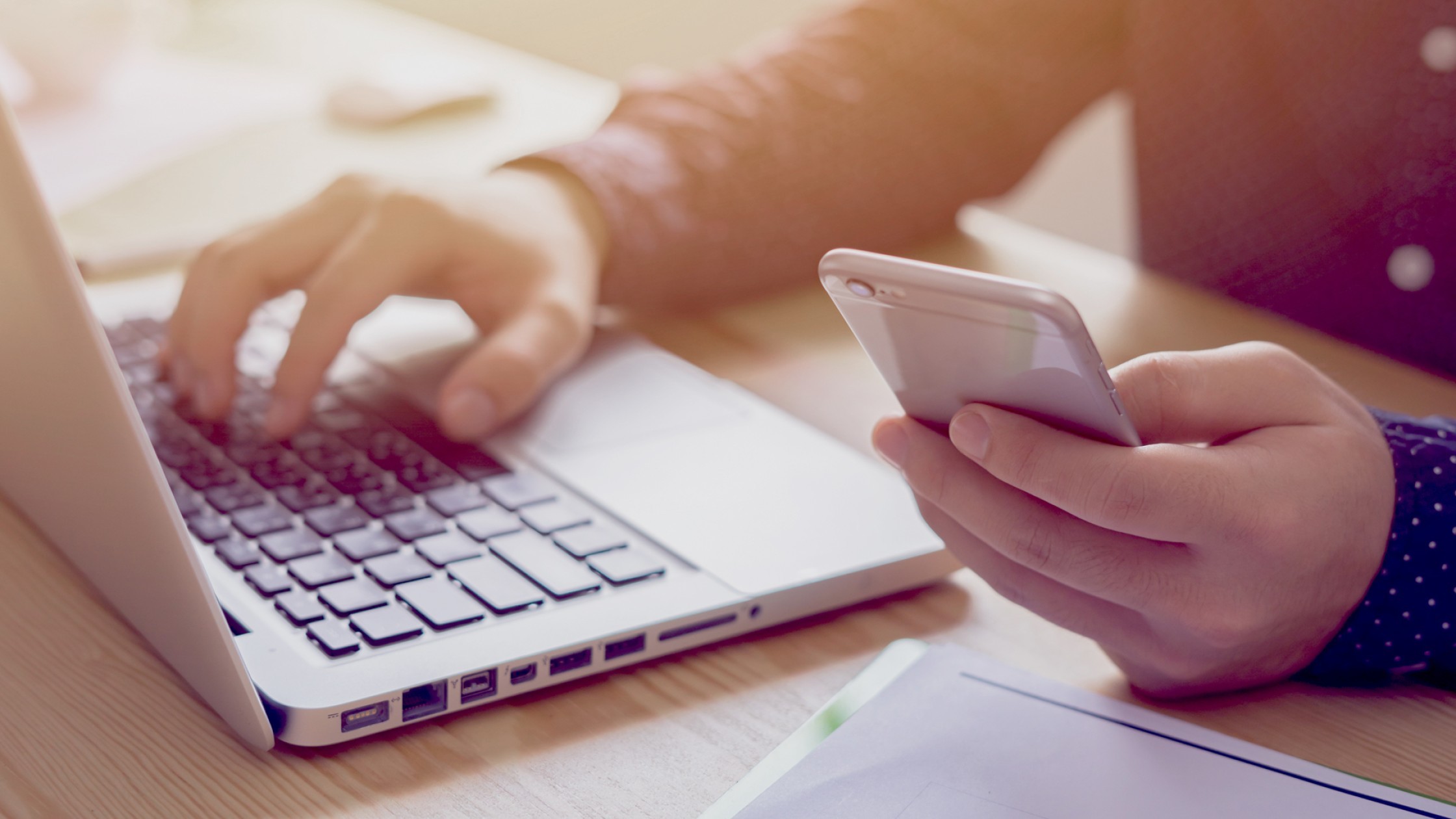 Nahaufnahme von Händen, die ein Smartphone und einen Laptop nutzen