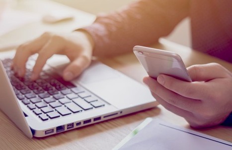 Nahaufnahme von Händen, die ein Smartphone und einen Laptop nutzen