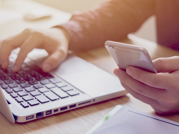 Nahaufnahme von Händen, die ein Smartphone und einen Laptop nutzen