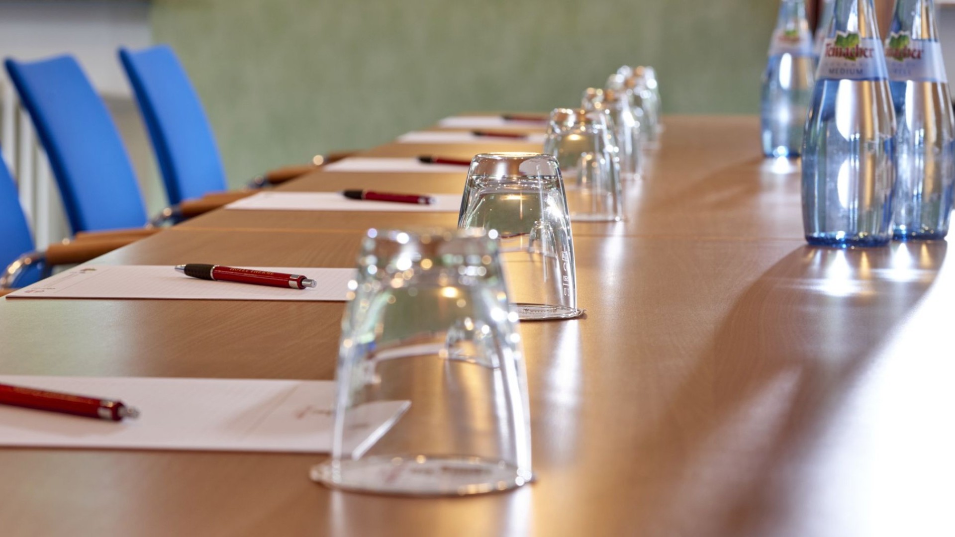 Moderner Konferenztisch mit Gläsern, Stiften und Schreibblöcken für Business-Meetings