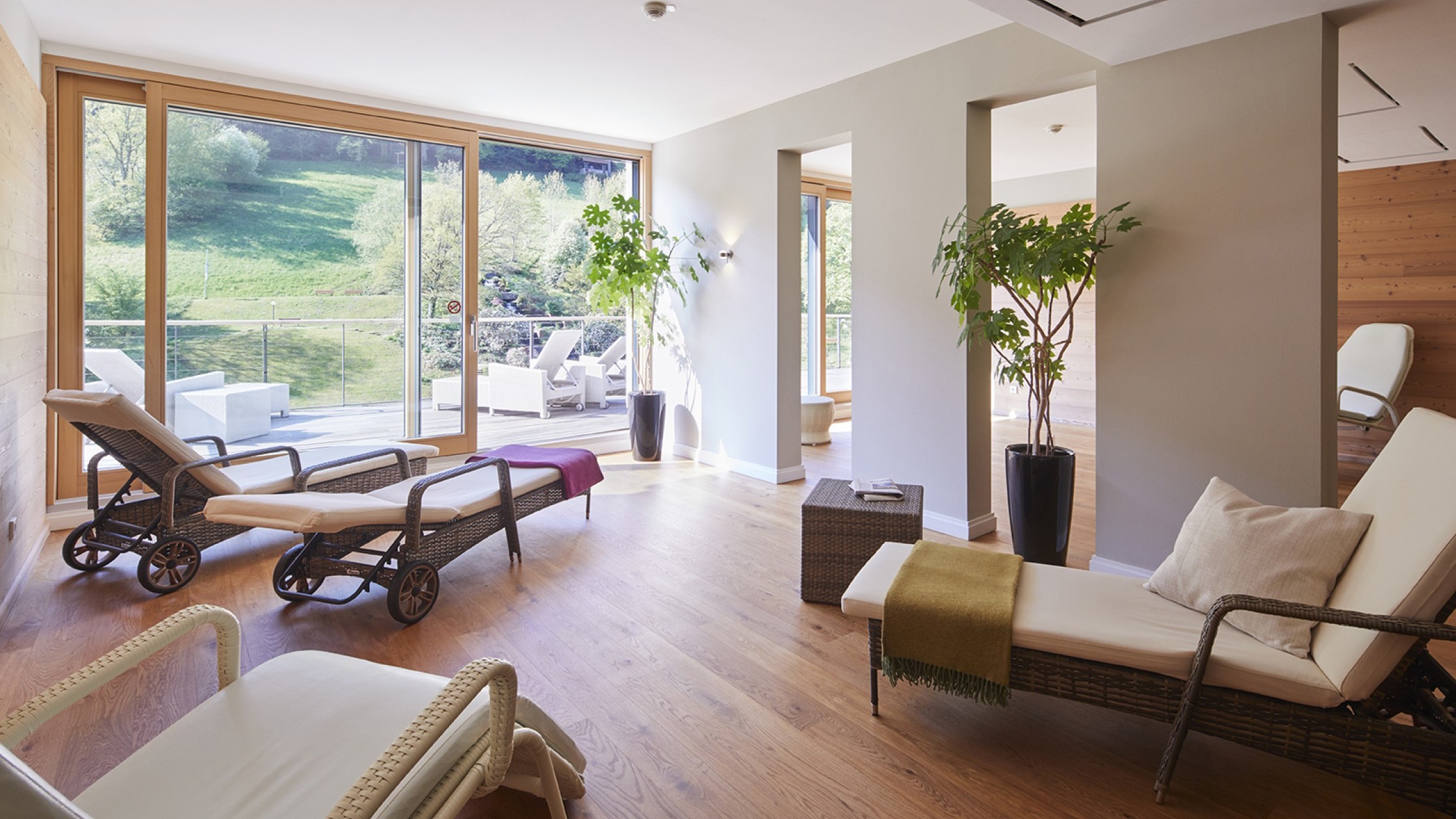 Heller Ruheraum im Panorama-Spa mit Holzliegen, Decken und Blick ins Grüne