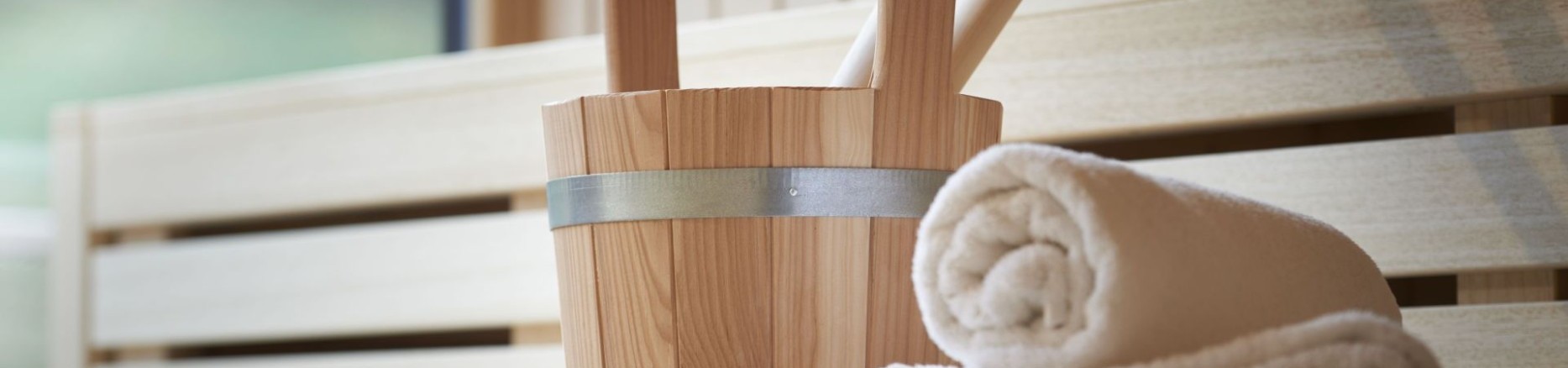 Saunaaufgusskübel mit Handtuch auf heller Holzbank