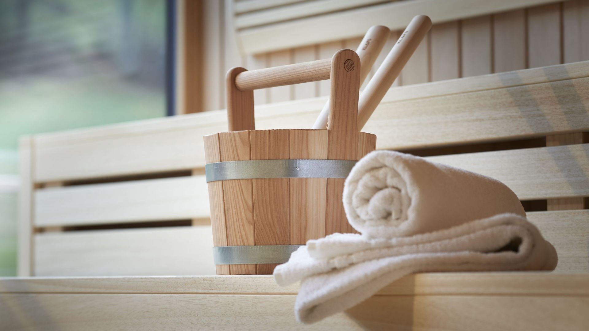 Saunaaufgusskübel mit Handtuch auf heller Holzbank