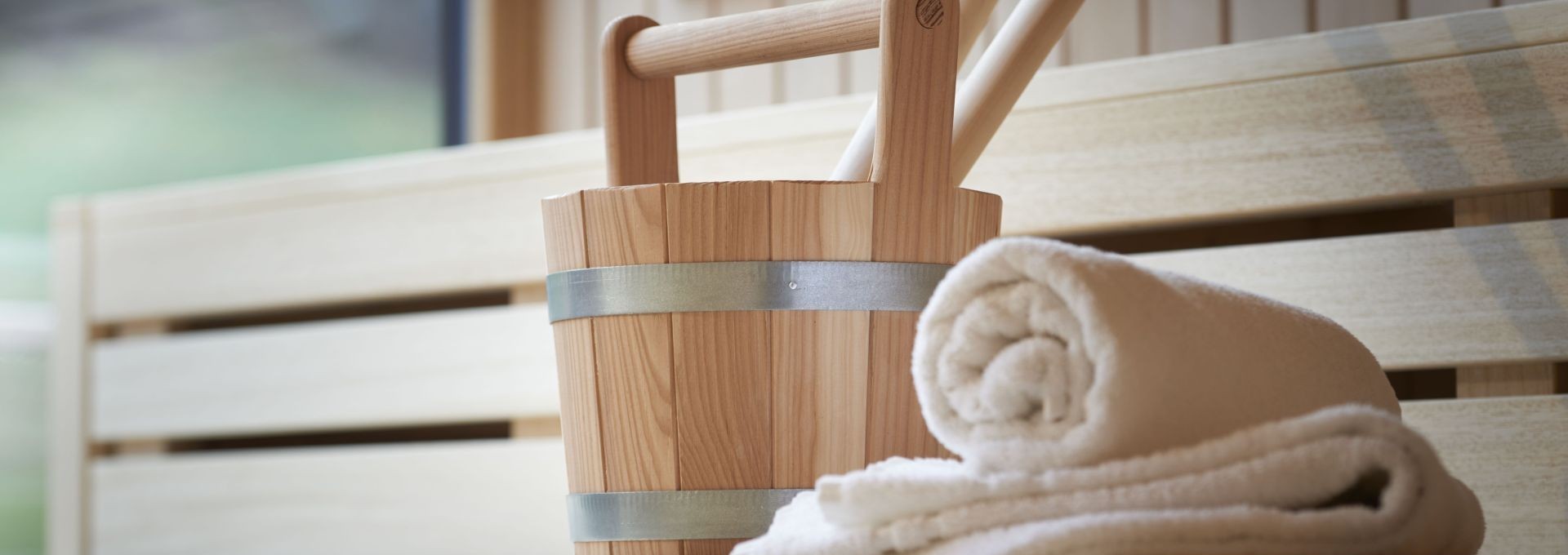 Saunaaufgusskübel mit Handtuch auf heller Holzbank