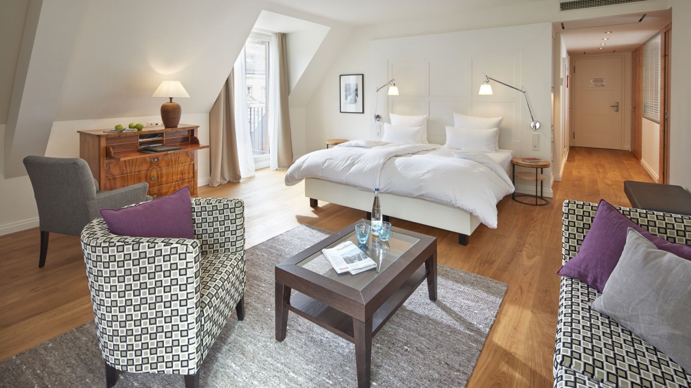 Helles und modernes Hotelzimmer mit gemütlicher Sitzecke und Doppelbett