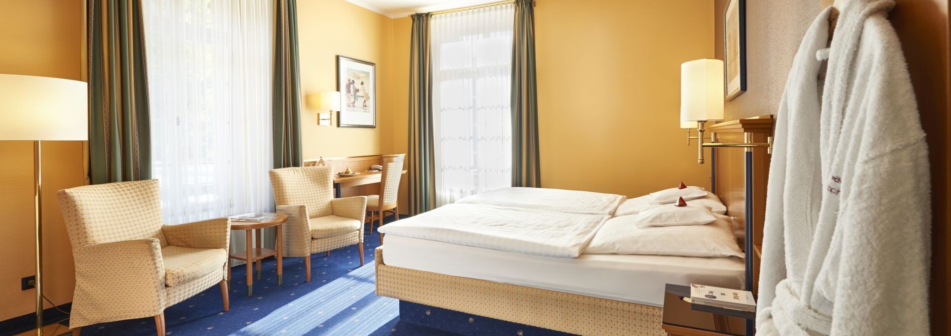 Doppelzimmer mit blauen Teppichboden, Sitzbereich und Tageslicht