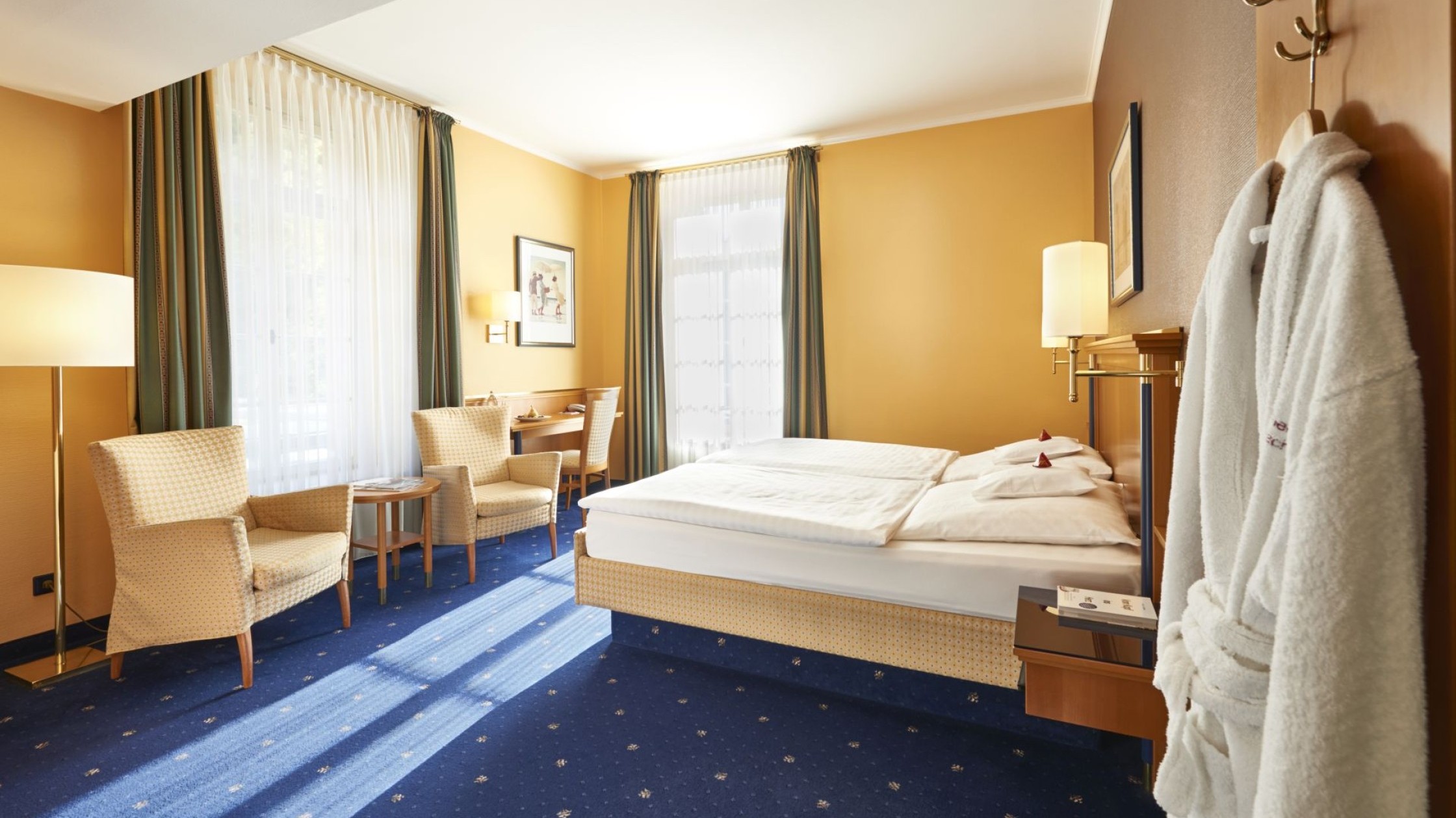 Doppelzimmer mit blauen Teppichboden, Sitzbereich und Tageslicht