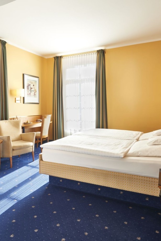 Doppelzimmer mit blauen Teppichboden, Sitzbereich und Tageslicht