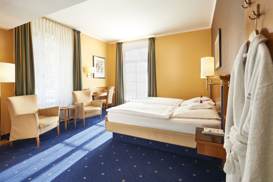 Doppelzimmer mit blauen Teppichboden, Sitzbereich und Tageslicht