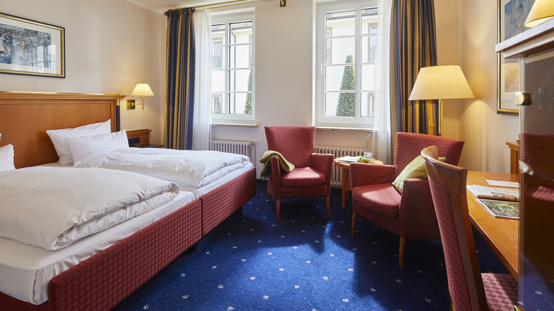 Gemütliches Doppelzimmer mit Sitzecke, blauen Teppich und Tageslicht