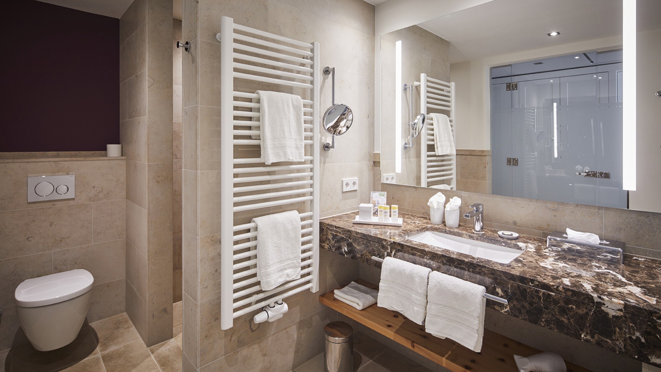 Helles Badezimmer mit Marmorwaschtisch, beleuchtetem Spiegel und großer Dusche