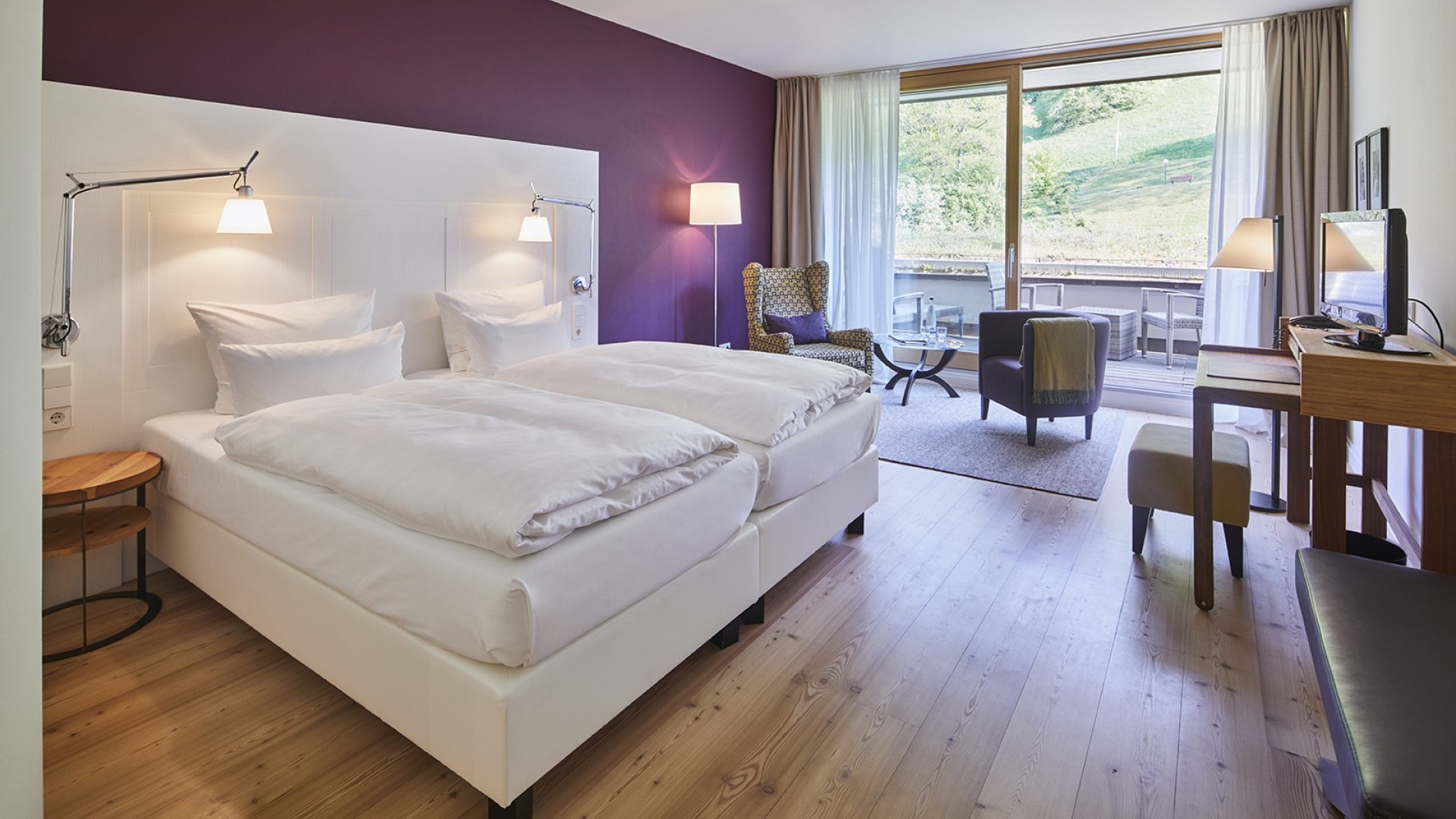 Komfortables Doppelzimmer mit lila Akzentwand und Balkon