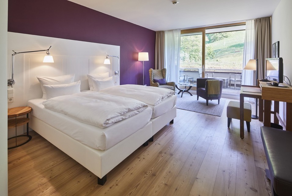 Komfortables Doppelzimmer mit lila Akzentwand und Balkon