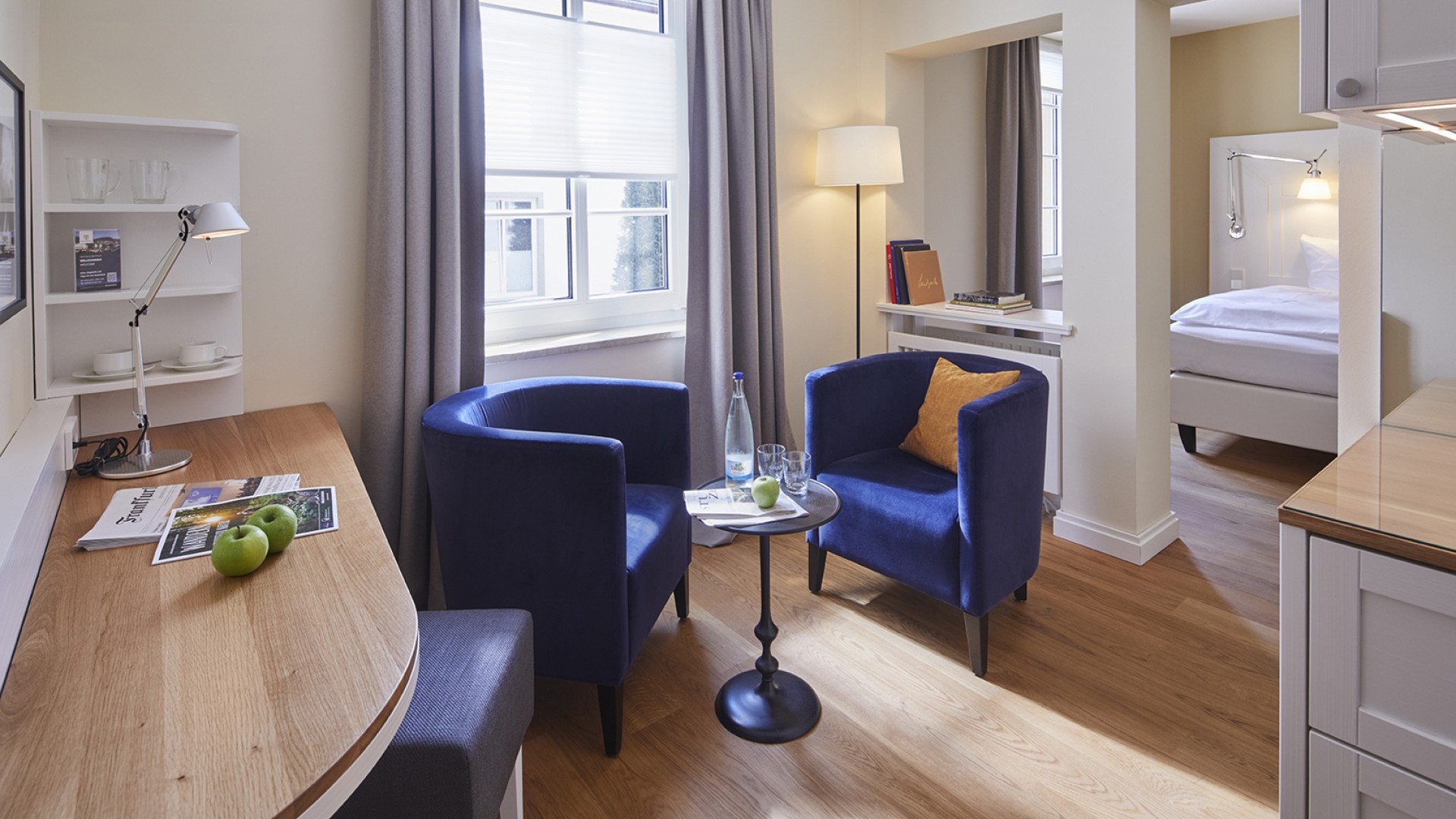 Moderner Sitzbereich mit blauen Sesseln, Schreibtisch und Blick ins Schlafzimmer