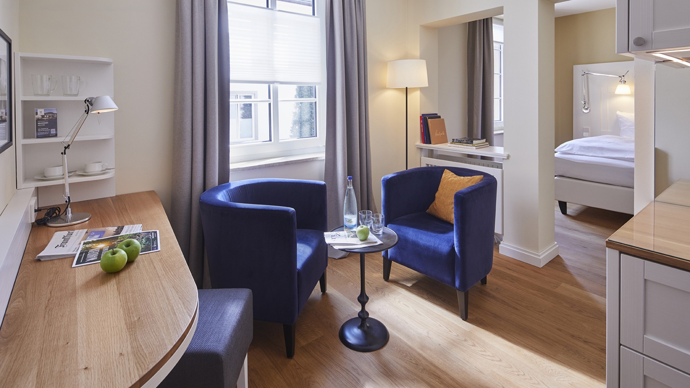 Moderner Sitzbereich mit blauen Sesseln, Schreibtisch und Blick ins Schlafzimmer