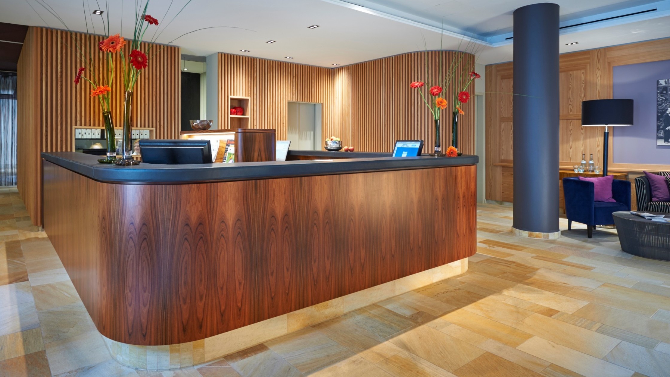 Rezeption mit geschwungener Holztheke und frischen Blumenarrangements